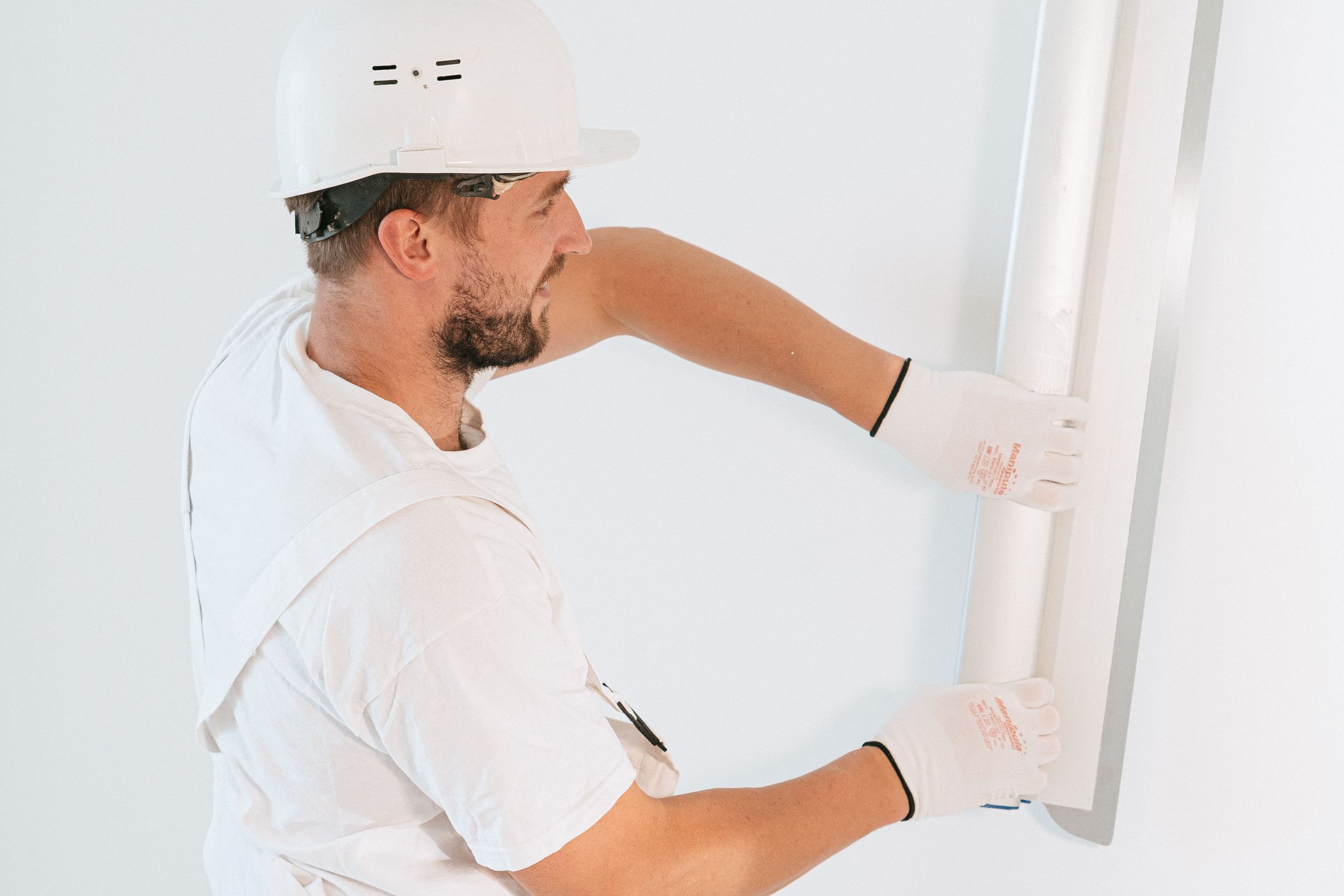 A construction worker installing drywall with gloves and a helmet