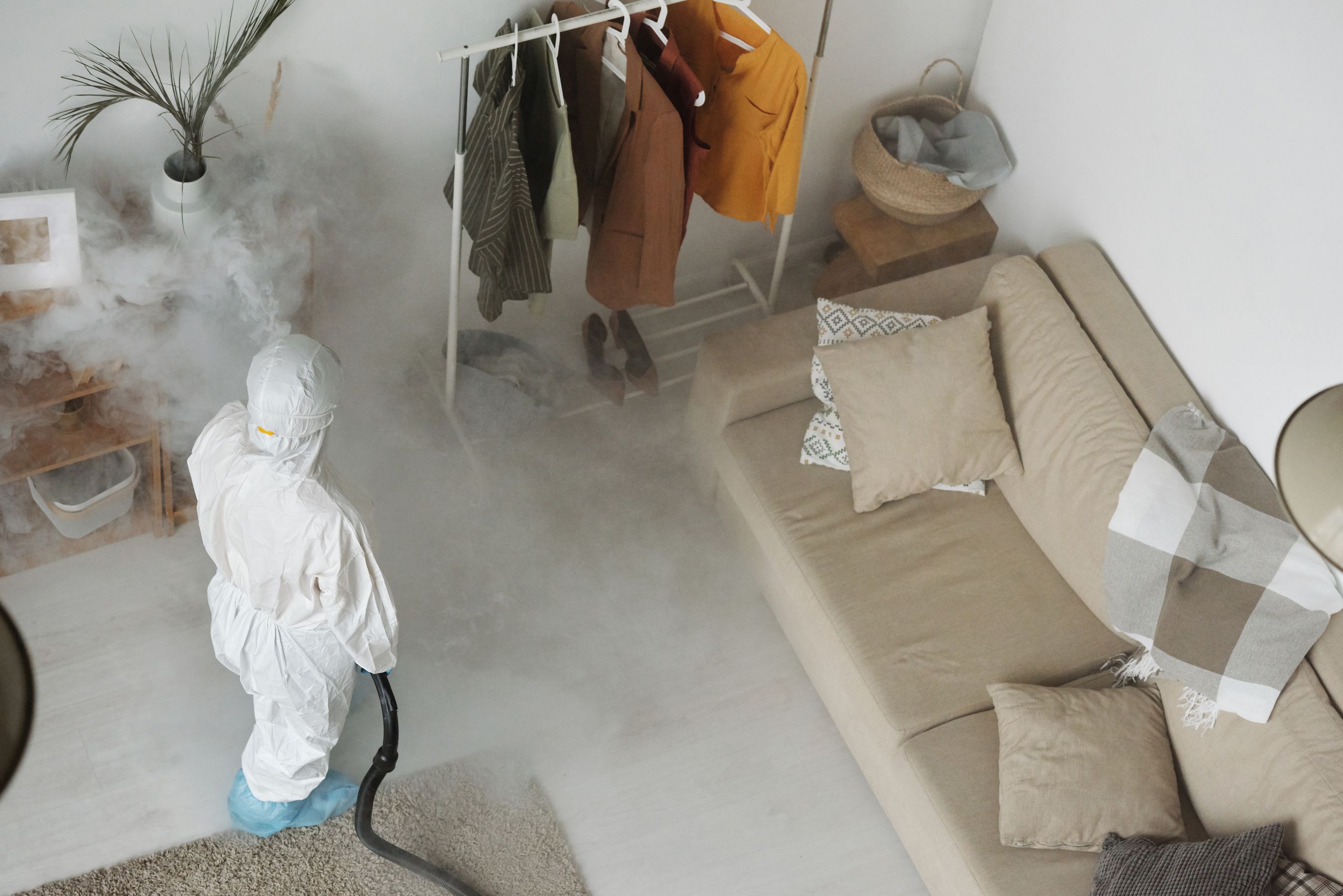 A pest control professional in protective gear sanitizing a modern living room