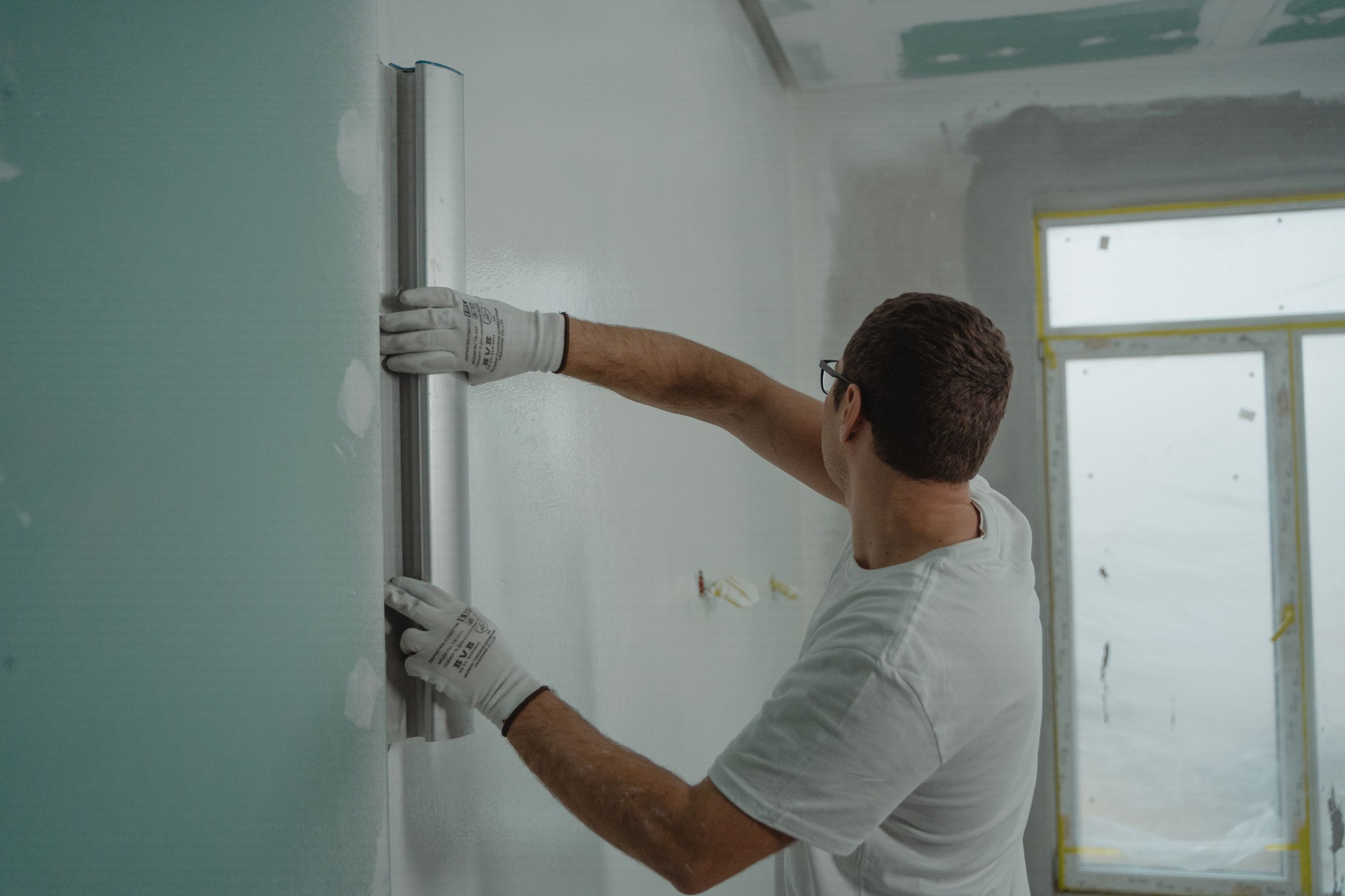A worker using a metal ruler for indoor wall renovation work