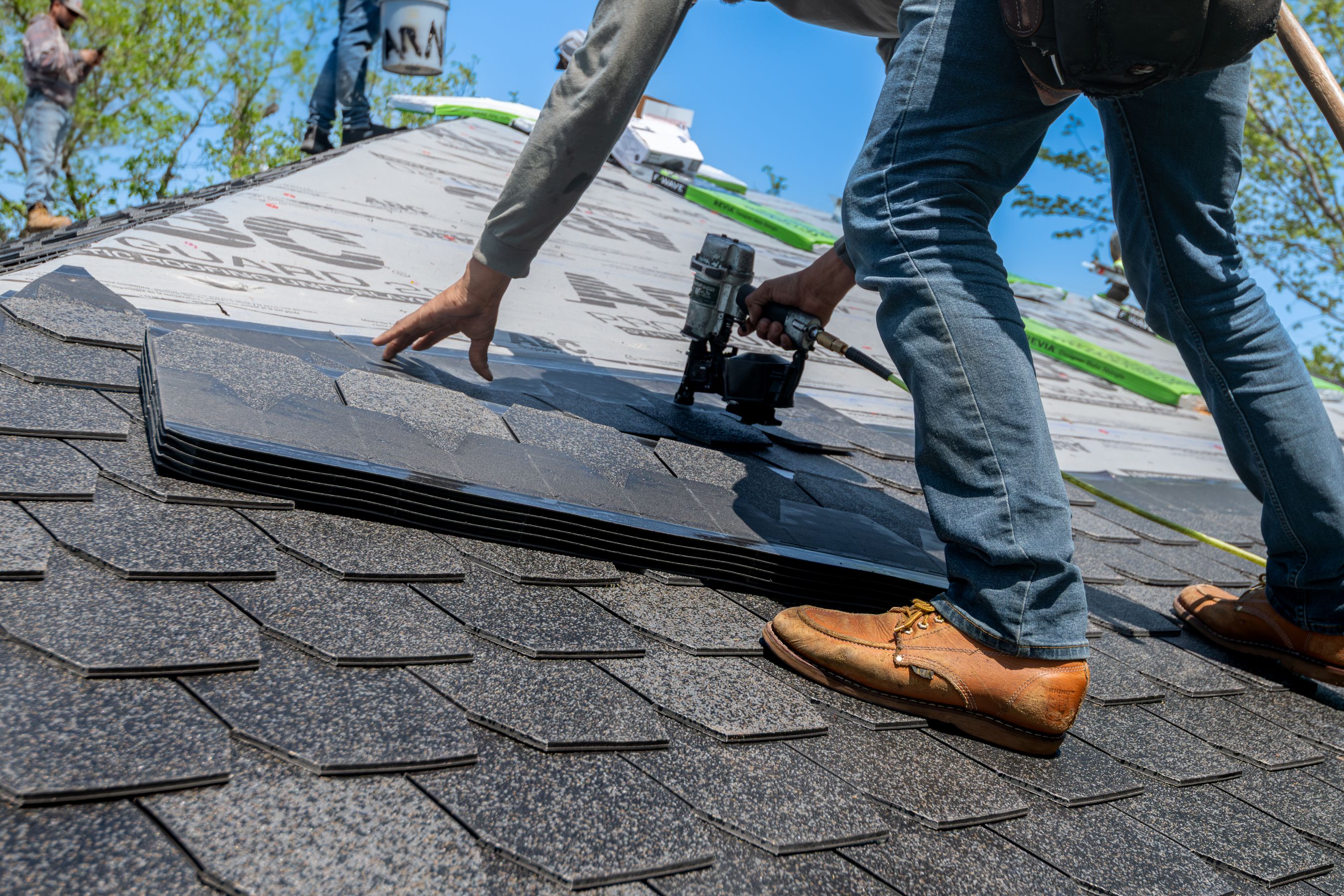 A roofer using a nail gun for shingle installation on a residential roof